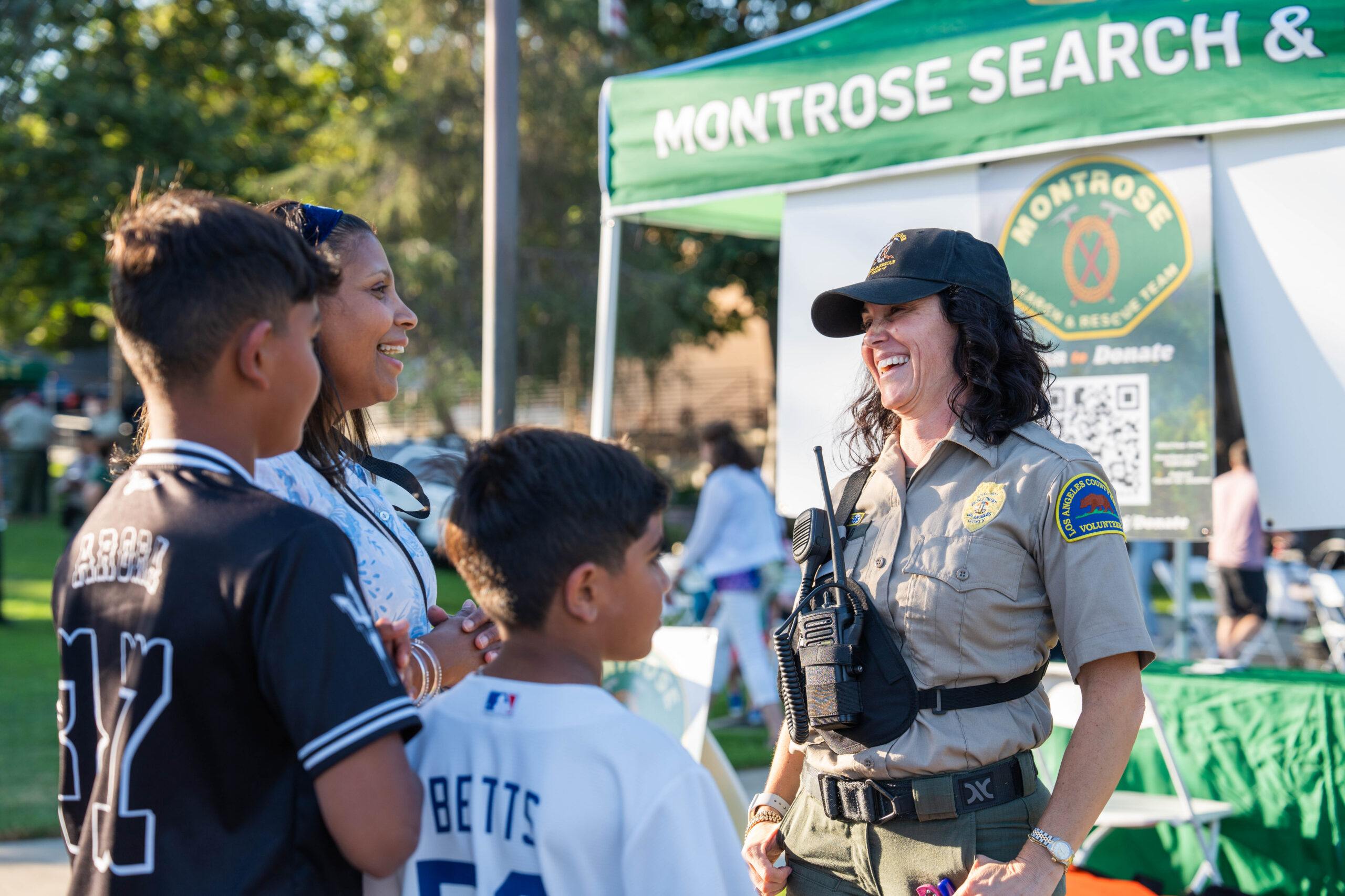 A search and rescue volunteer smiling while speaking with a family at an outreach booth.
